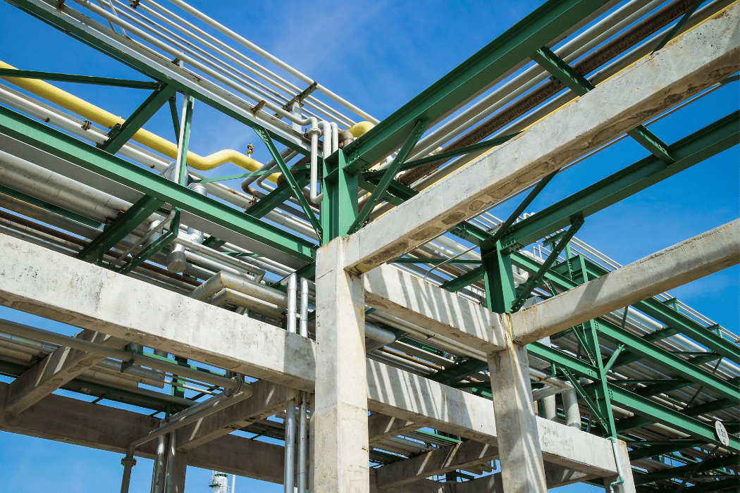 Industrial steel framework supporting an array of variously colored pipes under a blue sky, indicative of a chemical or processing plant infrastructure.
