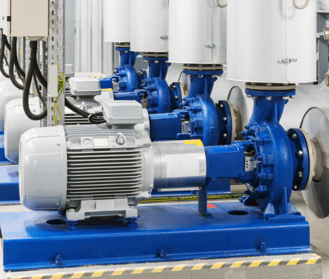 Industrial electric water pumps with blue housing and silver motors mounted on a blue base with yellow and black safety striping, in a mechanical room.