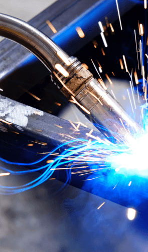 Dynamic close-up of arc welding on a steel beam, with sparks and blue light from the welding process, highlighting industrial fabrication techniques.