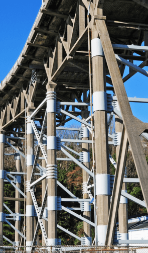 Tall steel bridge support structure with crisscrossing beams and white reinforced braces, showcasing civil engineering and construction against a clear sky.