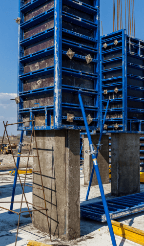 Concrete column being retrofitted with blue reinforced steel formwork, indicative of strengthening work on a construction site under a bright blue sky.