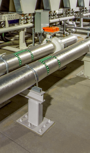 Insulated metal piping supported by steel structures, with valves and pressure meters in an industrial setting.
